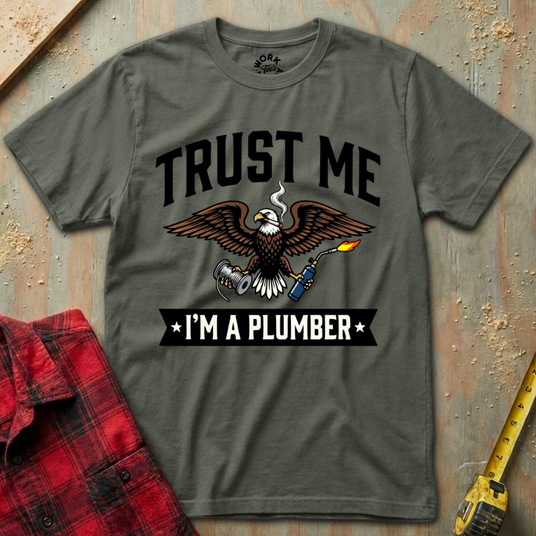 Gray t-shirt with eagle graphic and text 'Trust Me I'm a Plumber' on a textured surface.