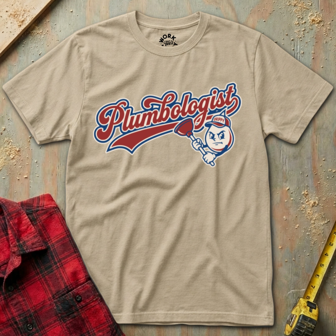 Beige t-shirt with 'Plumbologist' graphic design on a textured surface with plaid shirt and tape measure.