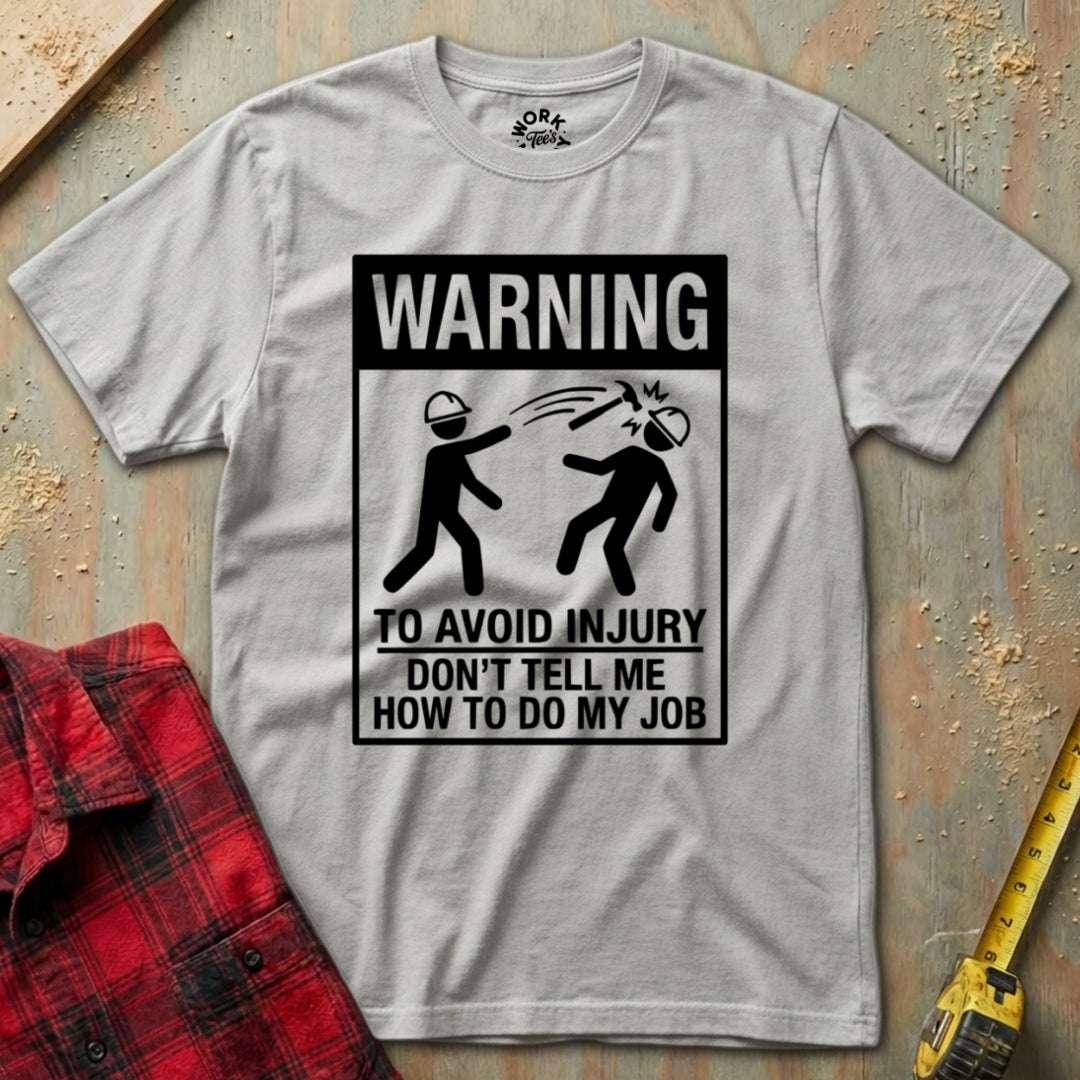 Gray t-shirt with a humorous warning graphic on a textured surface with a red plaid shirt and yellow tool in the background.