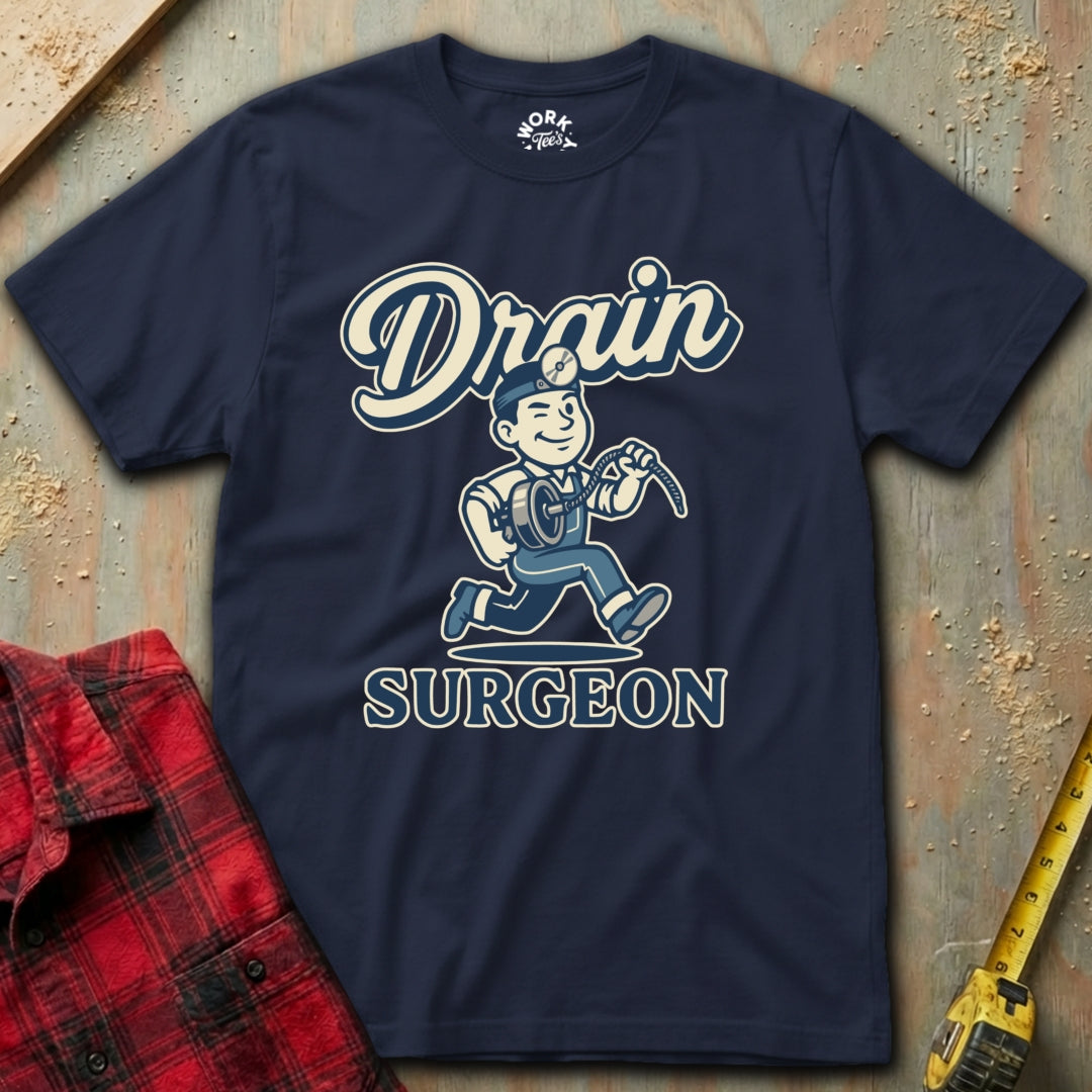 Navy blue t-shirt with 'Drain Surgeon' graphic design on a textured surface with tools.