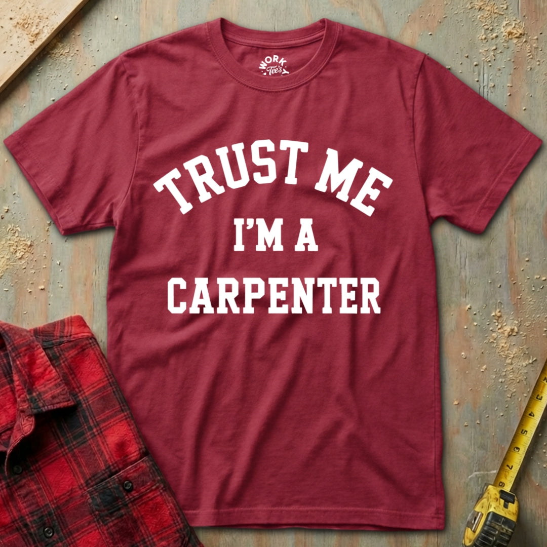Red t-shirt with 'Trust Me I'm a Carpenter' text on a textured surface with a plaid shirt and tape measure.
