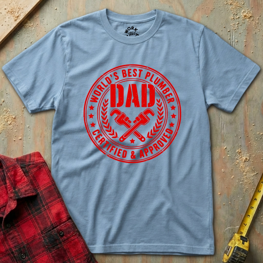 Gray t-shirt with red 'World's Best Plumber Dad' graphic on a wooden surface with tools.