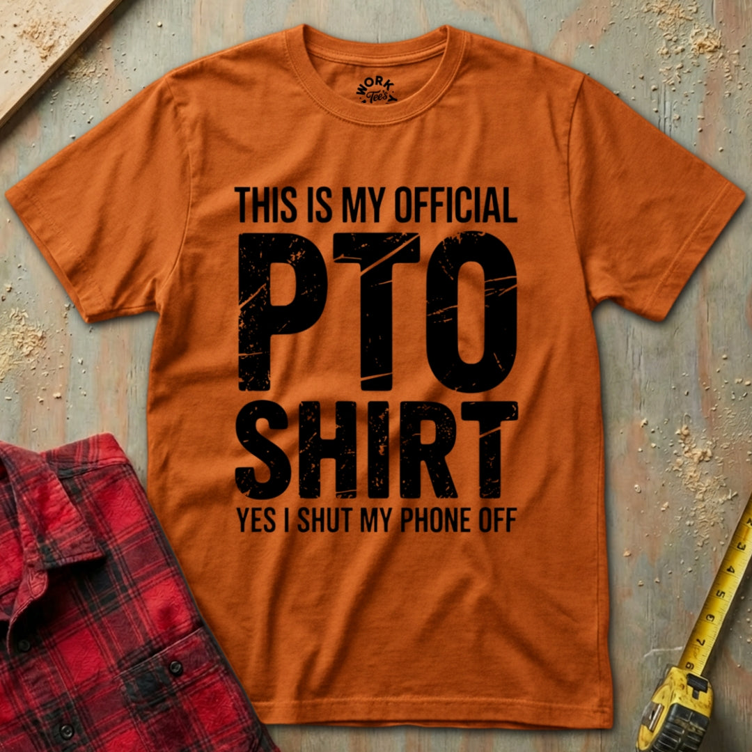 Orange t-shirt with black text on a textured surface with a red plaid shirt and yellow tool in the background.