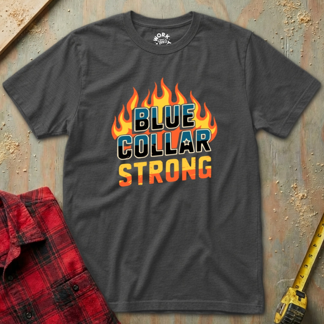 Gray t-shirt with 'Blue Collar Strong' graphic on a textured surface with a red plaid shirt and yellow tool in the background.