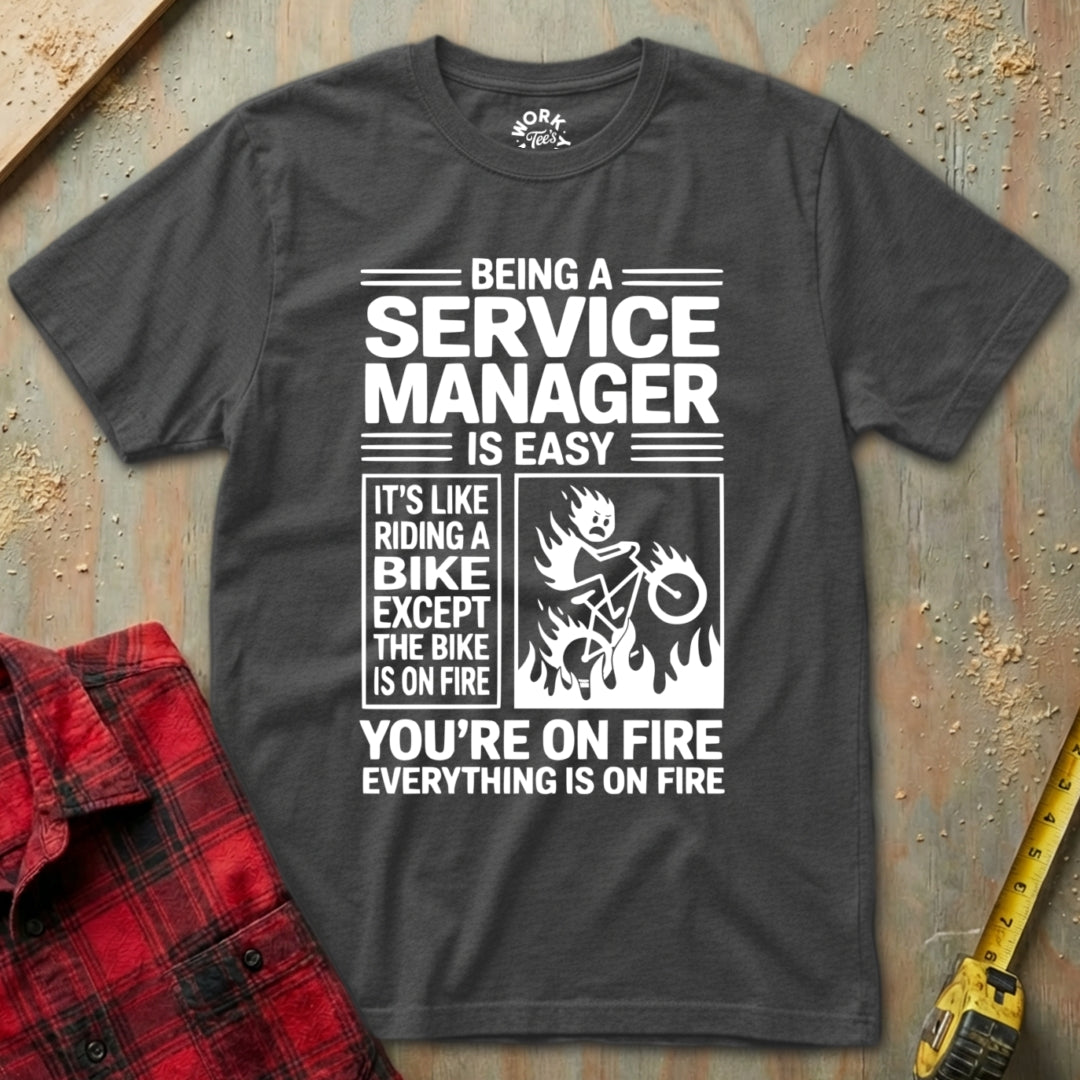 Gray t-shirt with humorous text design on a textured surface with a red plaid shirt and yellow tool in the background.