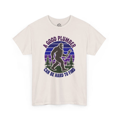 Beige t-shirt with a graphic of a bigfoot holding a wrench and text 'A good plumber can be hard to find' on a white background.