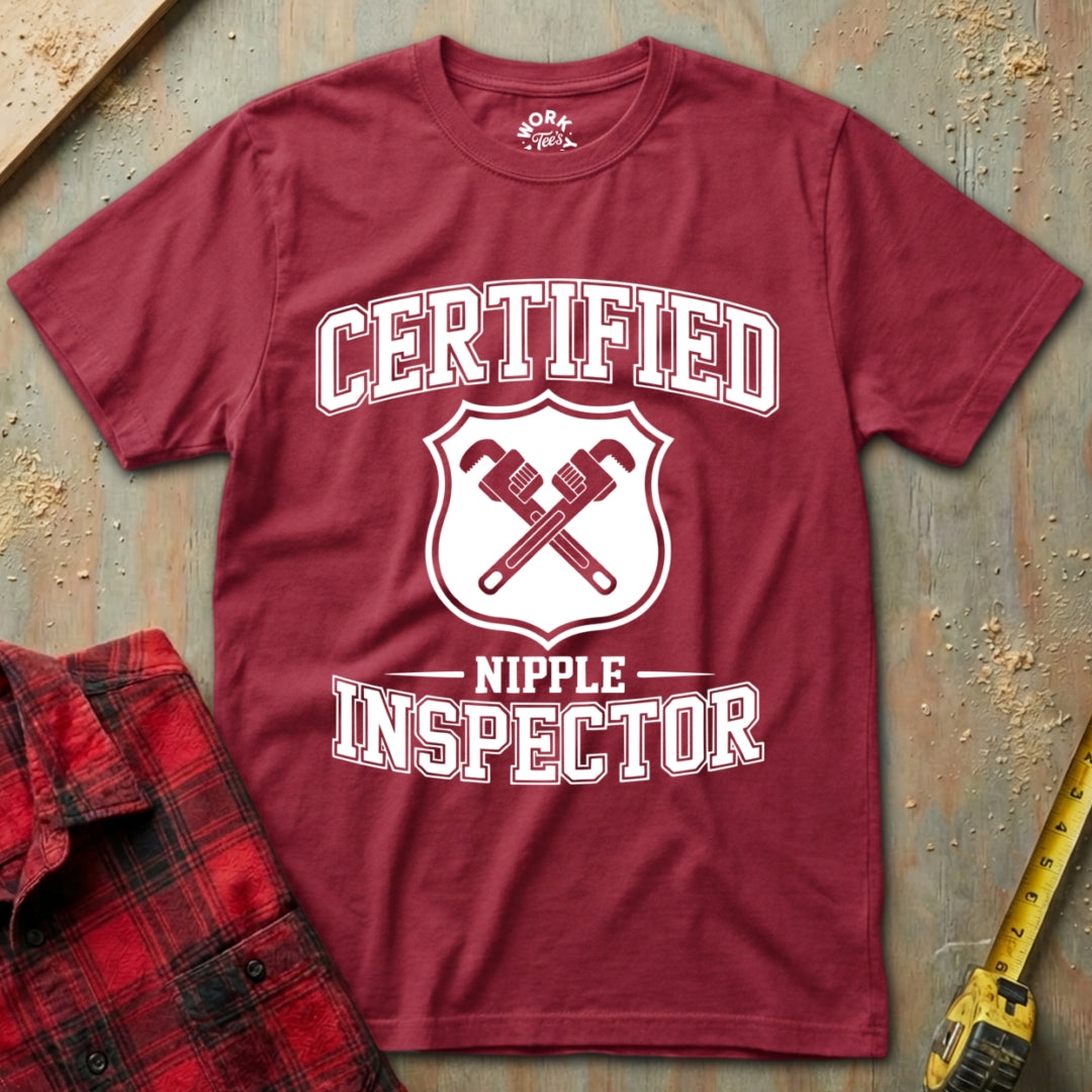 Red t-shirt with 'Certified Nipple Inspector' text and graphic on a textured surface.