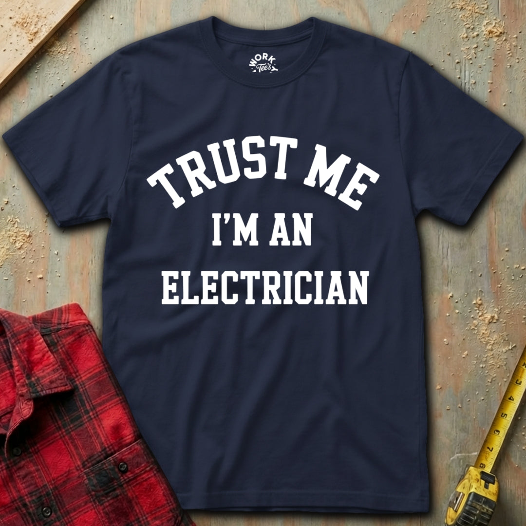 Navy blue t-shirt with 'Trust Me I'm an Electrician' text on a textured surface with tools.