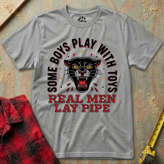 Gray t-shirt with a graphic design and text on a textured surface with a red flannel shirt and yellow tool in the background.