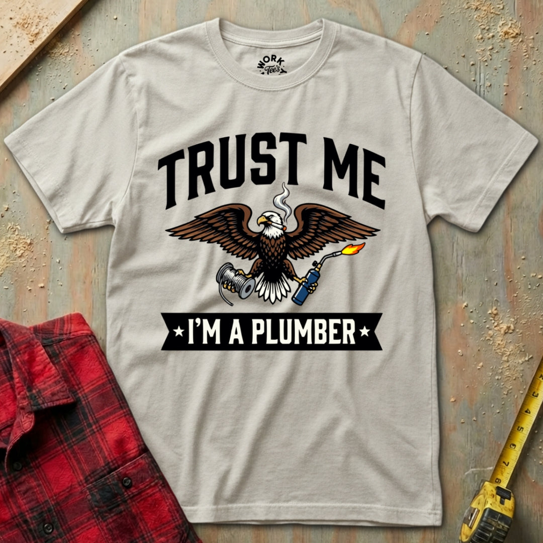 T-shirt with 'Trust Me, I'm a Plumber' graphic on a textured surface with tools.