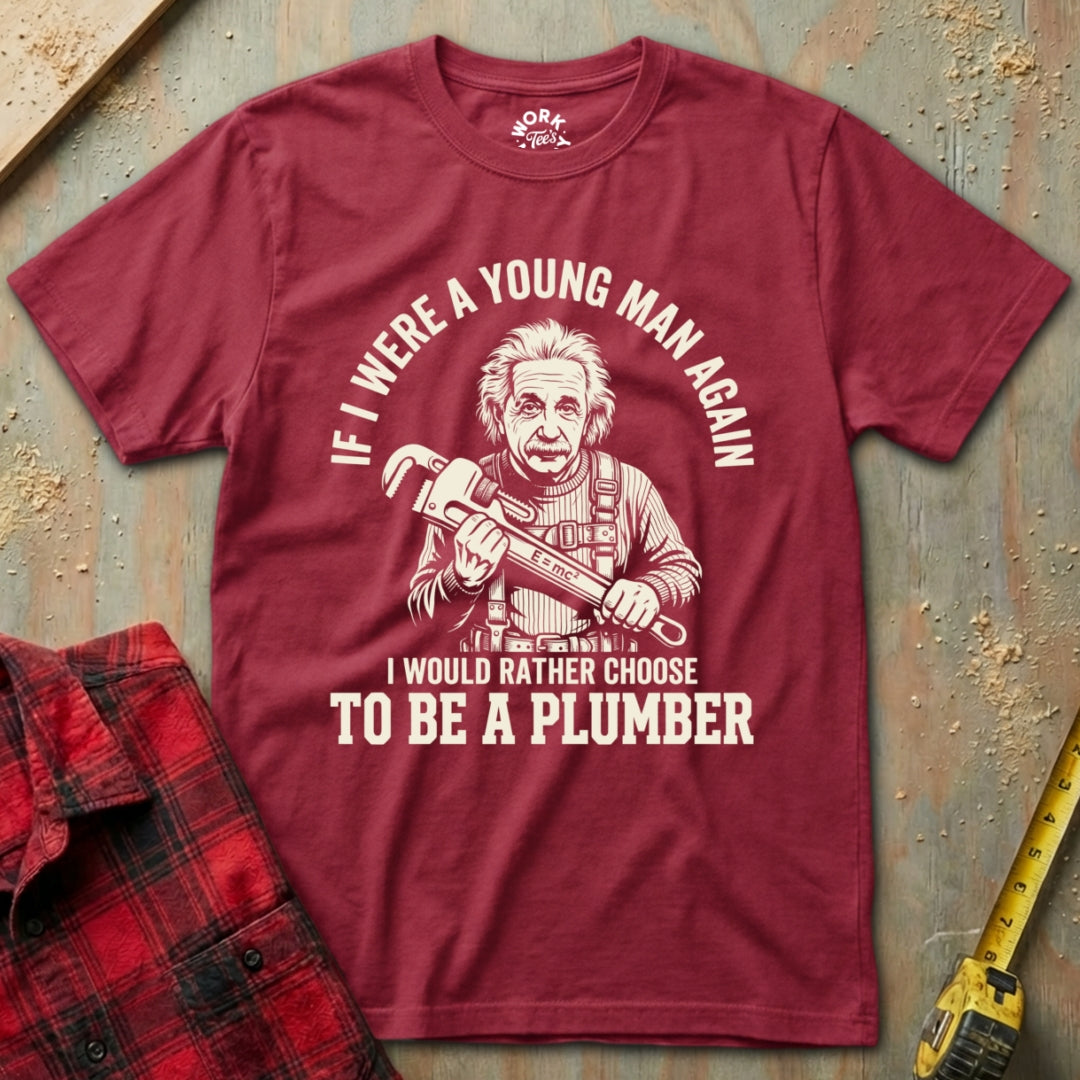 Maroon t-shirt with a graphic and text about choosing to be a plumber, placed on a textured surface with tools.