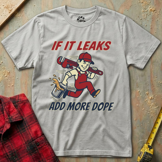 Gray t-shirt with a graphic of a plumber and text 'If it leaks add more dope' on a textured surface.