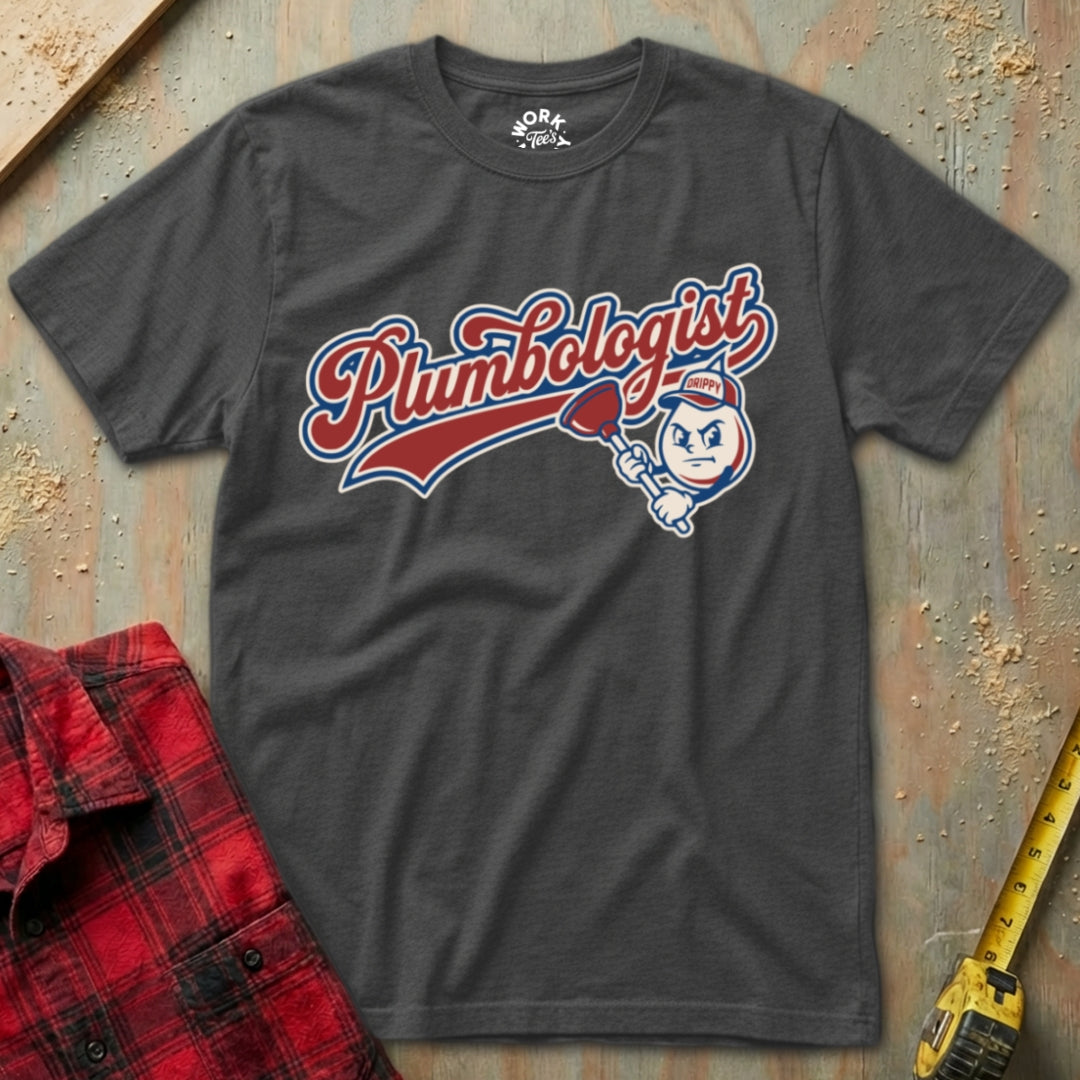 Gray t-shirt with 'Plumbologist' graphic on a textured surface with a red plaid shirt and yellow tool in the background.