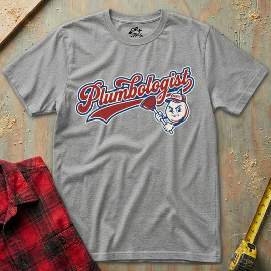 Gray t-shirt with 'Plumbologist' graphic on a textured surface with a red flannel shirt and yellow tool in the background.