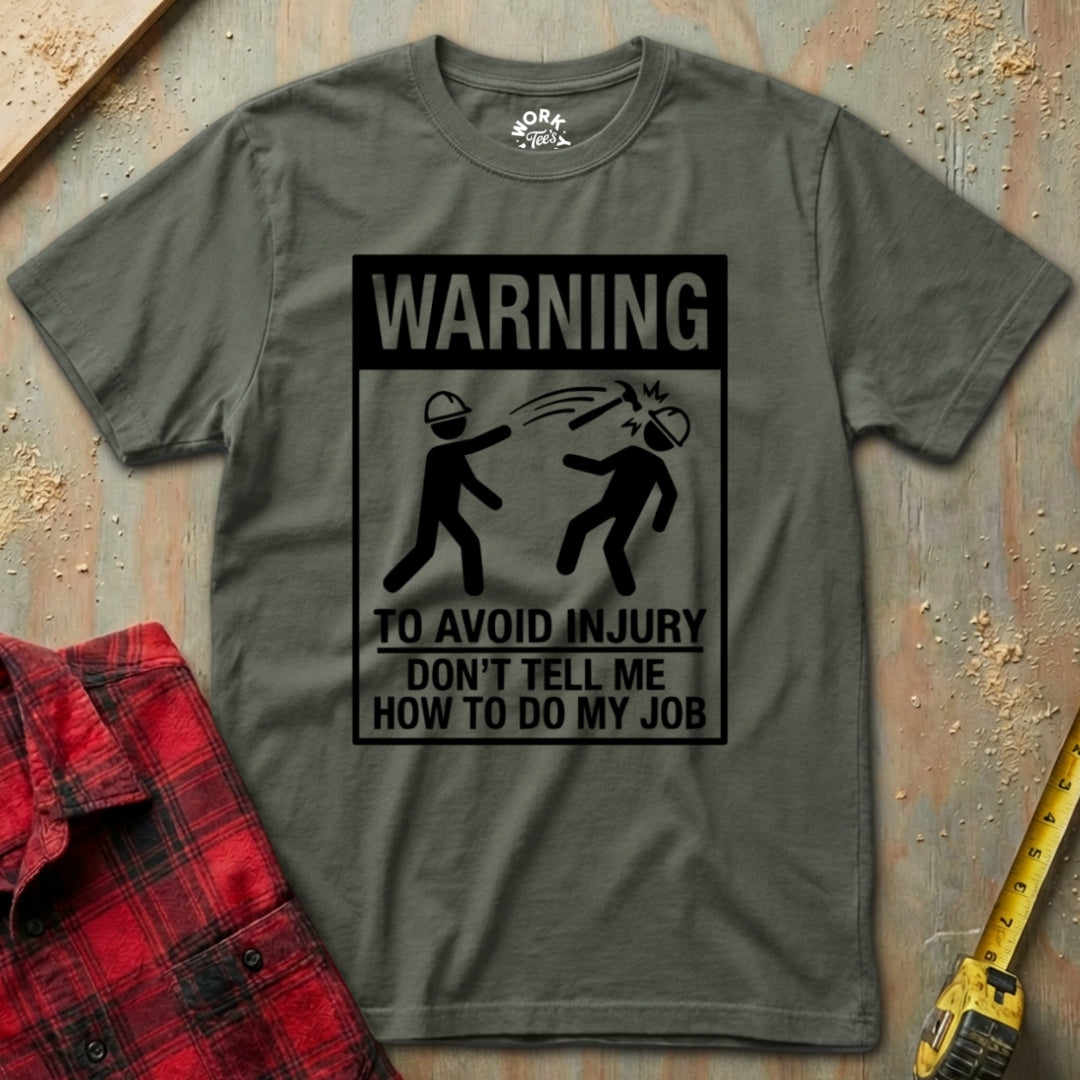 Military Green t-shirt with a humorous warning graphic on a textured surface with a red plaid shirt and yellow tool in the background.