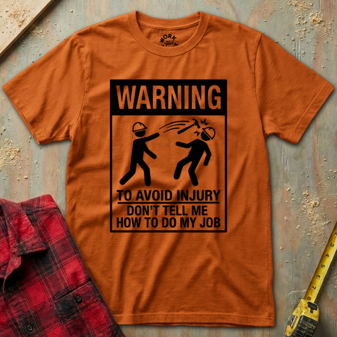 Orange t-shirt with a humorous warning graphic on a textured surface with tools.