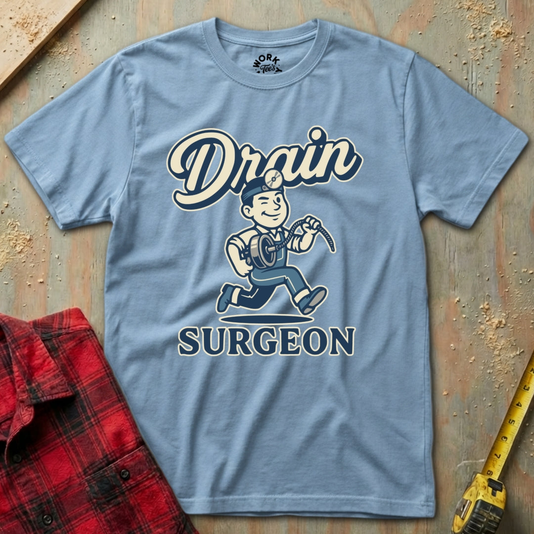 Blue t-shirt with 'Drain Surgeon' graphic on a wooden surface with tools.