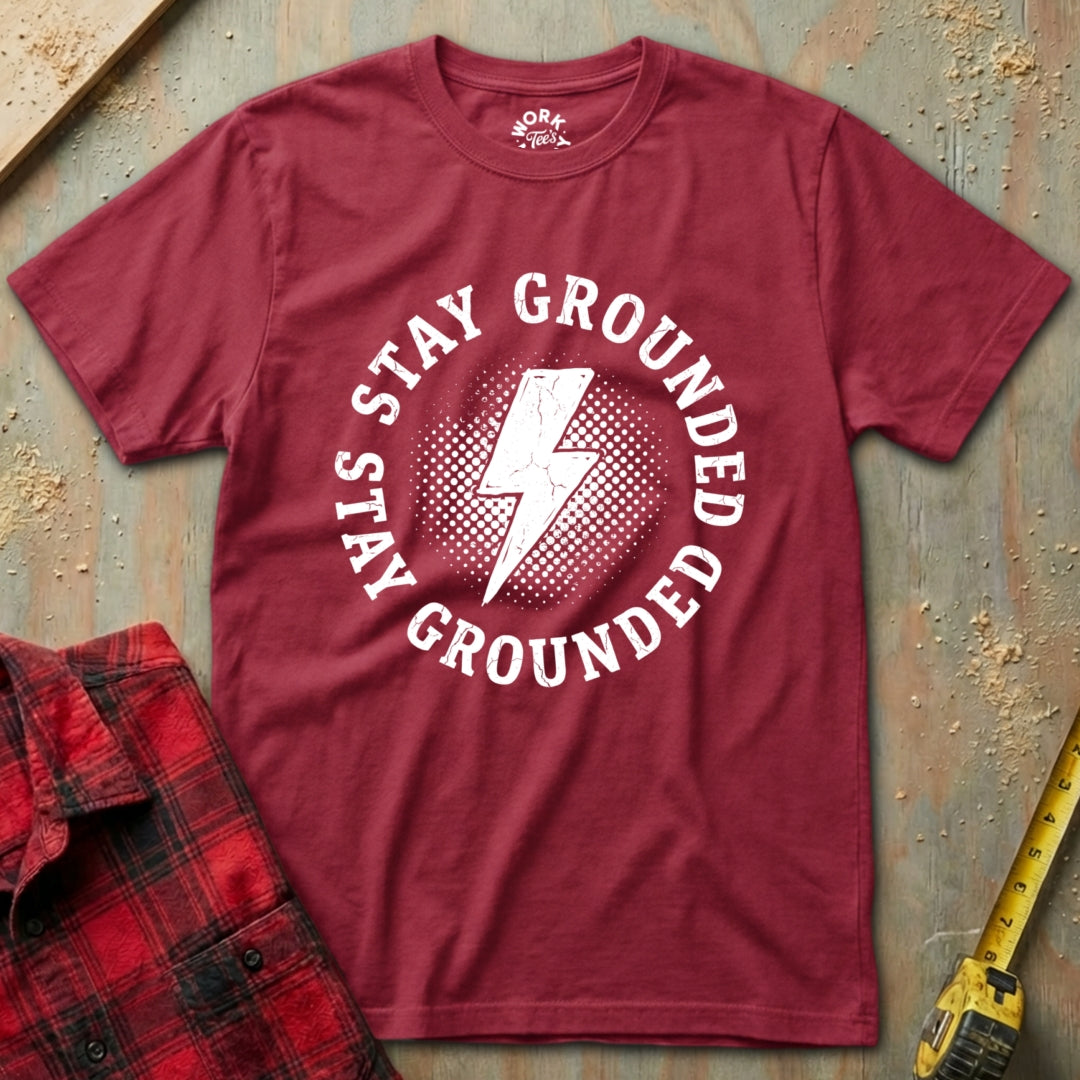 Red t-shirt with 'Stay Grounded' graphic on a textured surface with plaid shirt and tape measure.