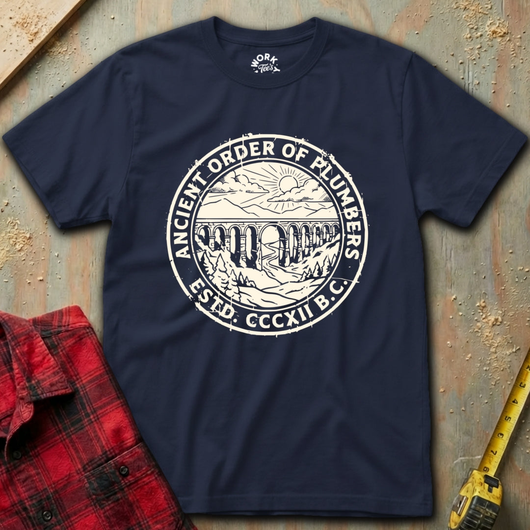 Navy blue t-shirt with 'Ancient Order of Plumbers' logo on a textured surface with tools.