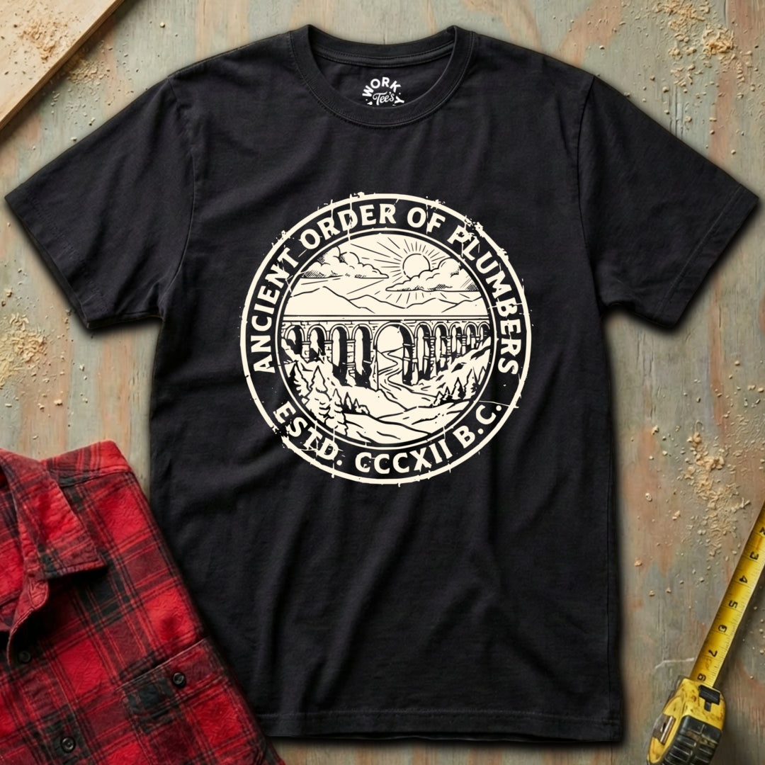Black t-shirt with 'Ancient Order of Plumbers' logo on a textured surface with red plaid shirt and yellow tool in background