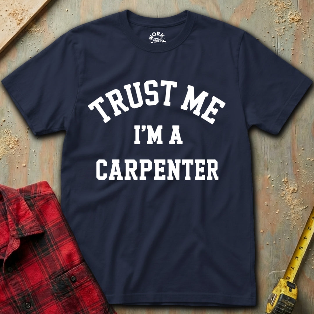 Navy blue t-shirt with 'Trust Me I'm a Carpenter' text on a wooden background with a red plaid shirt and yellow tape measure.