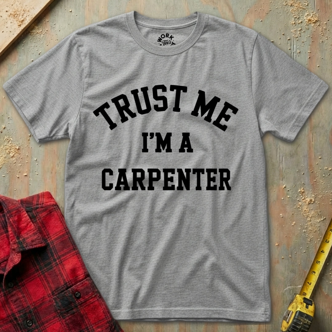 Gray t-shirt with 'Trust Me I'm a Carpenter' text on a wooden background with a red plaid shirt and yellow tape measure.