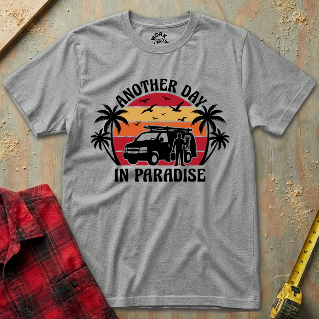 Gray t-shirt with 'Another Day in Paradise' graphic on a textured surface with plaid shirt and tape measure.