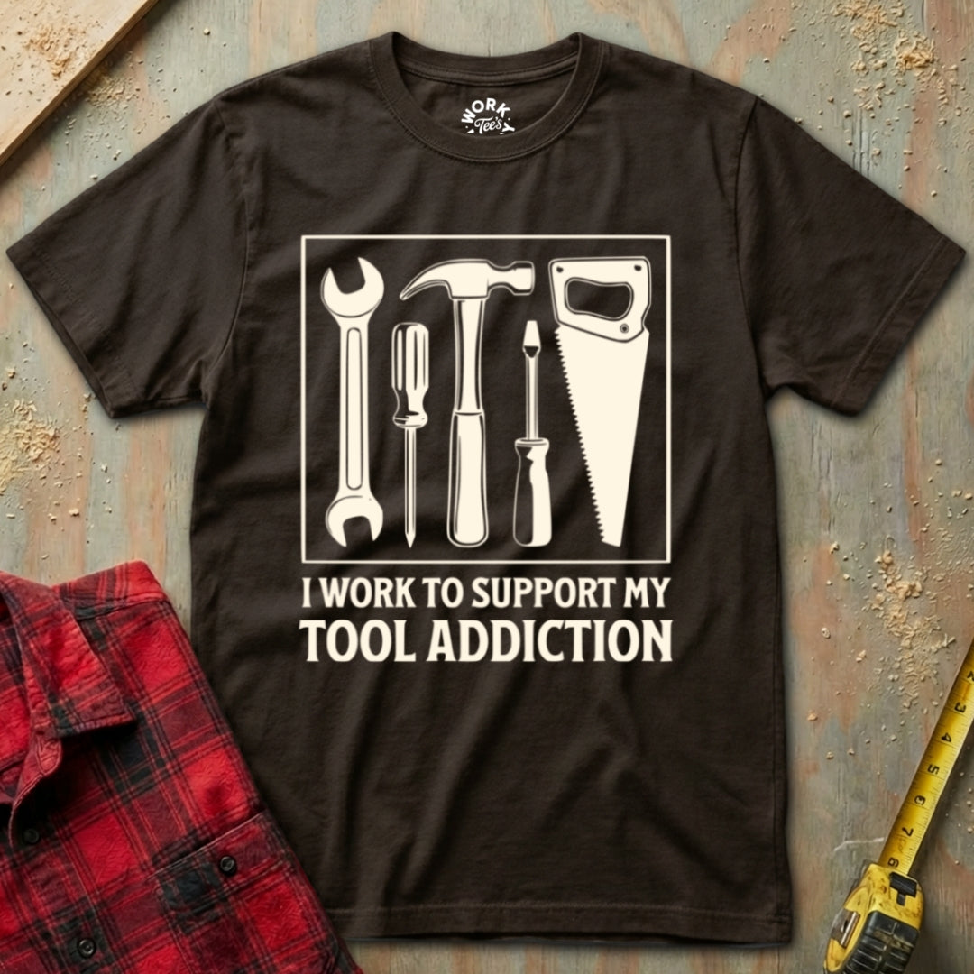 Brown t-shirt with tool graphic and text on a textured surface with plaid shirt and tape measure.