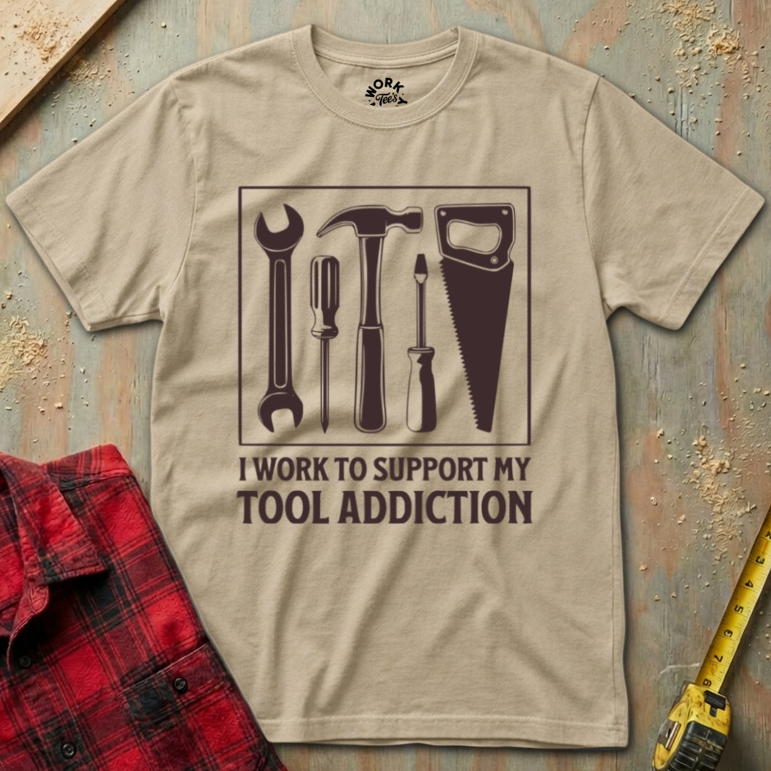 Beige t-shirt with tool graphic and text on a wooden surface with tools.