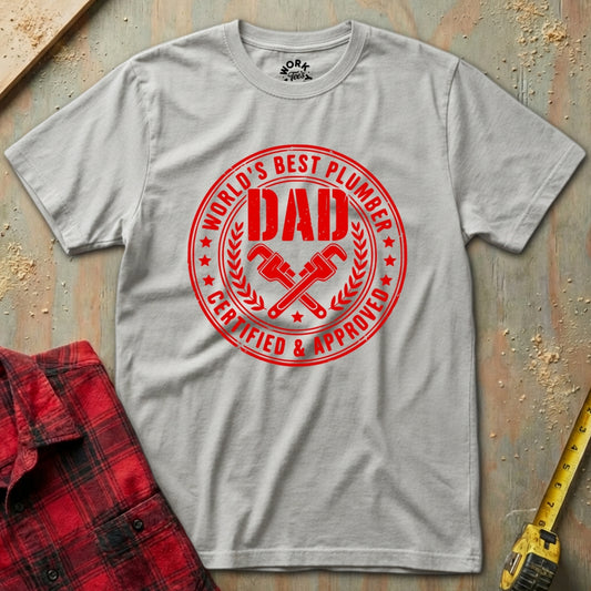 Gray t-shirt with red 'World's Best Plumber Dad' graphic on a wooden surface with tools.