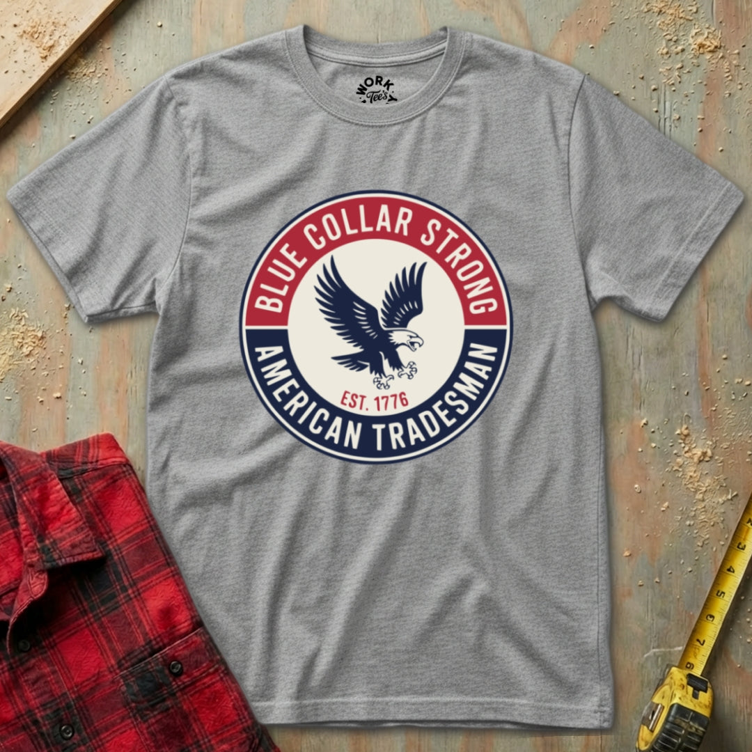 Gray t-shirt with 'Blue Collar Strong American Tradesman' logo on a textured surface with plaid shirt and tape measure.