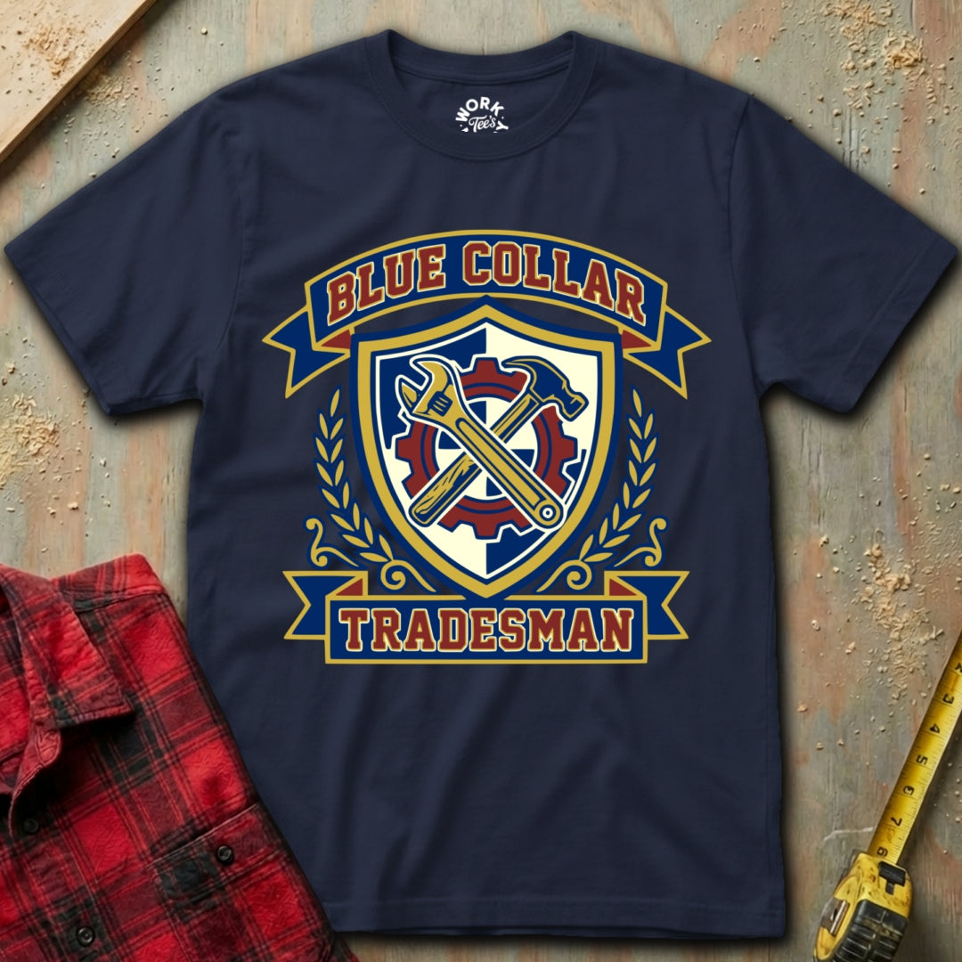Navy blue t-shirt with 'Blue Collar Tradesman' graphic on a textured surface with plaid shirt and tape measure.