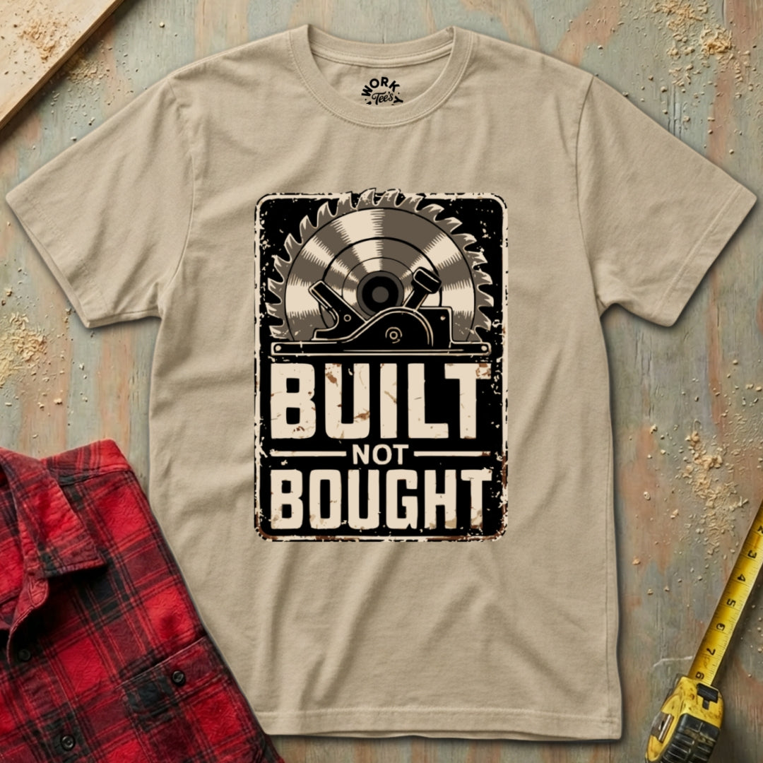 Beige t-shirt with 'Built Not Bought' graphic on a wooden background