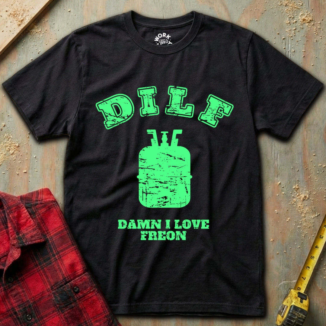 Black t-shirt with green graphic and text on a textured surface with a red plaid shirt and yellow tool in the background.