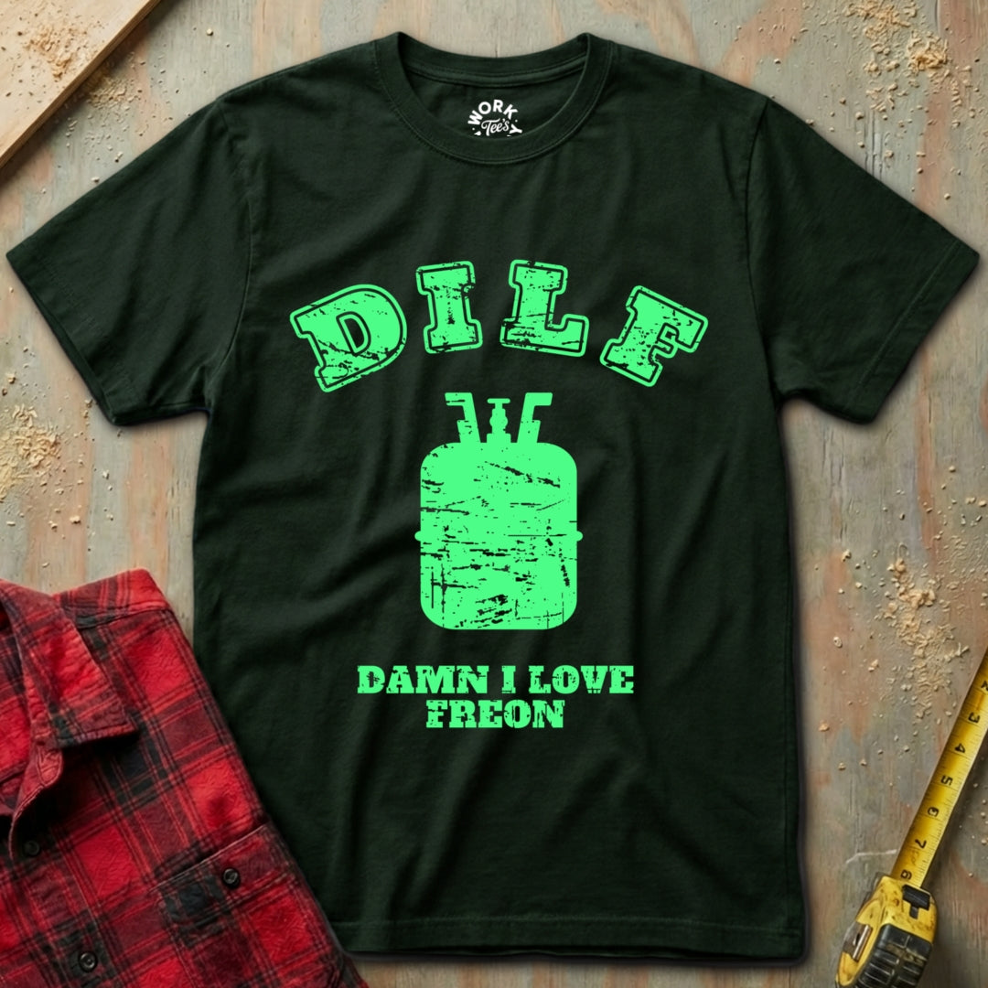 Black t-shirt with green text and graphics on a textured surface with a red plaid shirt and yellow tool in the background.