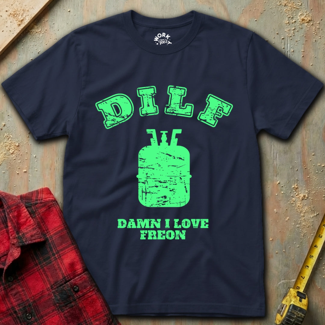 Navy blue t-shirt with green graphic and text on a textured surface with red plaid shirt and yellow tool in background