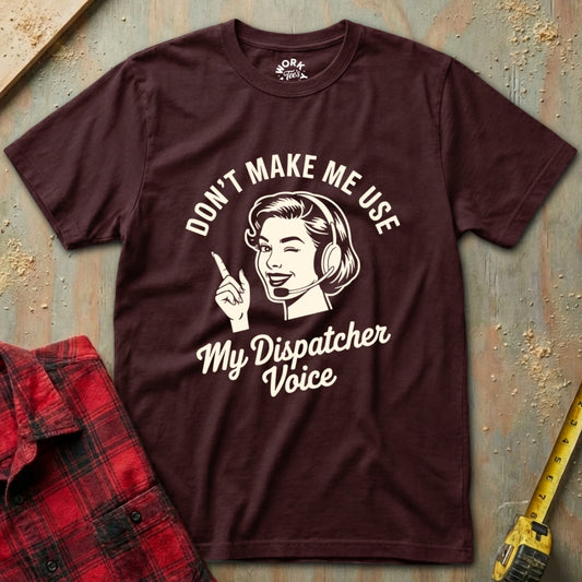 Brown t-shirt with graphic and text 'Don't Make Me Use My Dispatcher Voice' on a textured surface.