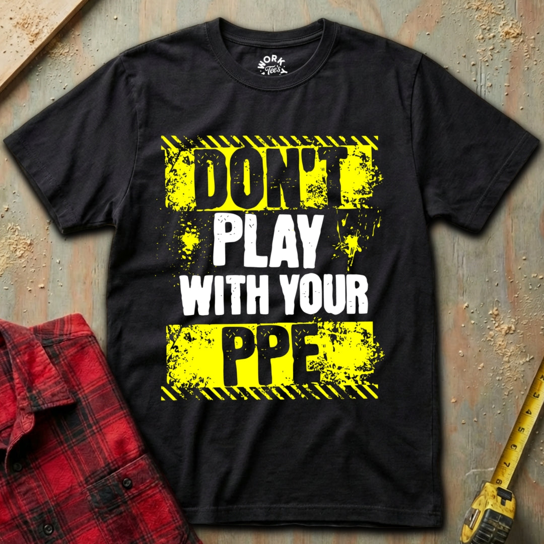 Black t-shirt with safety-themed text on a textured surface with a red plaid shirt and yellow tool.