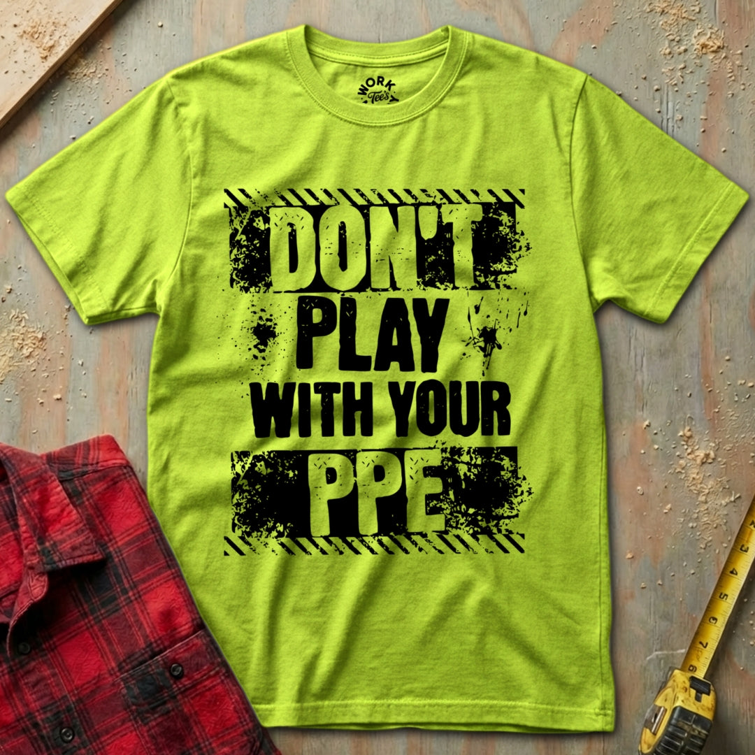 Green t-shirt with 'Don't Play with Your PPE' text on a textured surface with a red shirt and yellow tool in the background.
