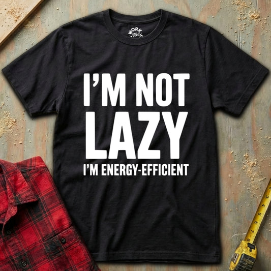 Black t-shirt with 'I'm not lazy, I'm energy-efficient' text on a textured surface with a red plaid shirt and yellow tool in the background.