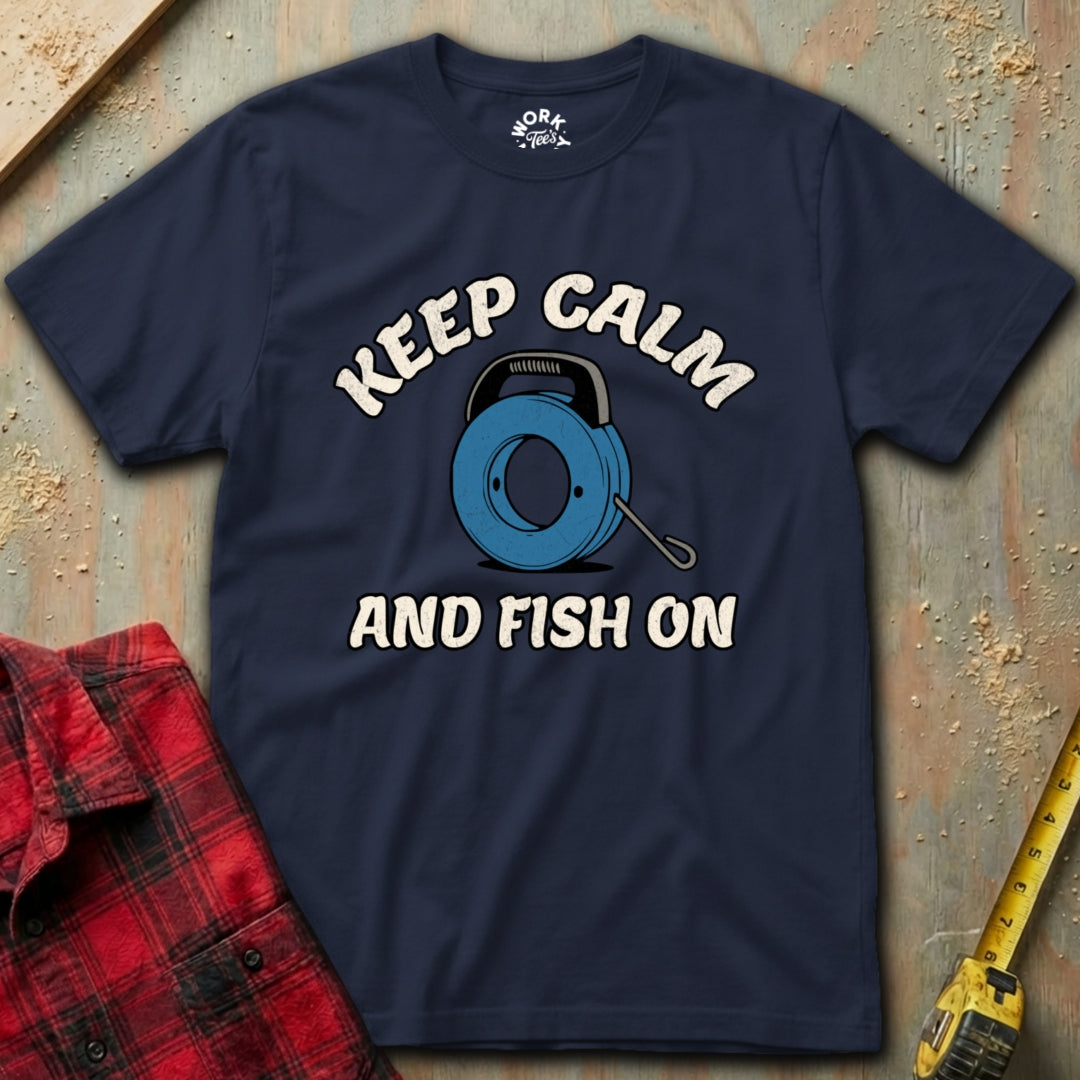 Navy blue t-shirt with 'Keep Calm and Fish On' graphic on a textured surface with plaid shirt and tape measure.