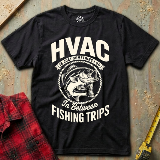 Black t-shirt with HVAC fishing graphic on a textured surface with plaid shirt and tape measure.