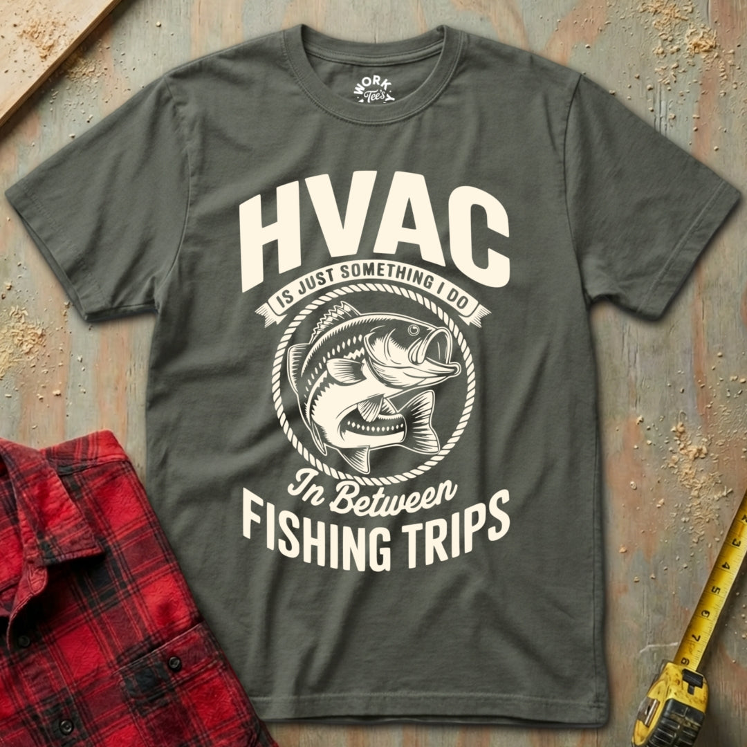 Gray t-shirt with HVAC fishing graphic on a textured surface with plaid shirt and tape measure.