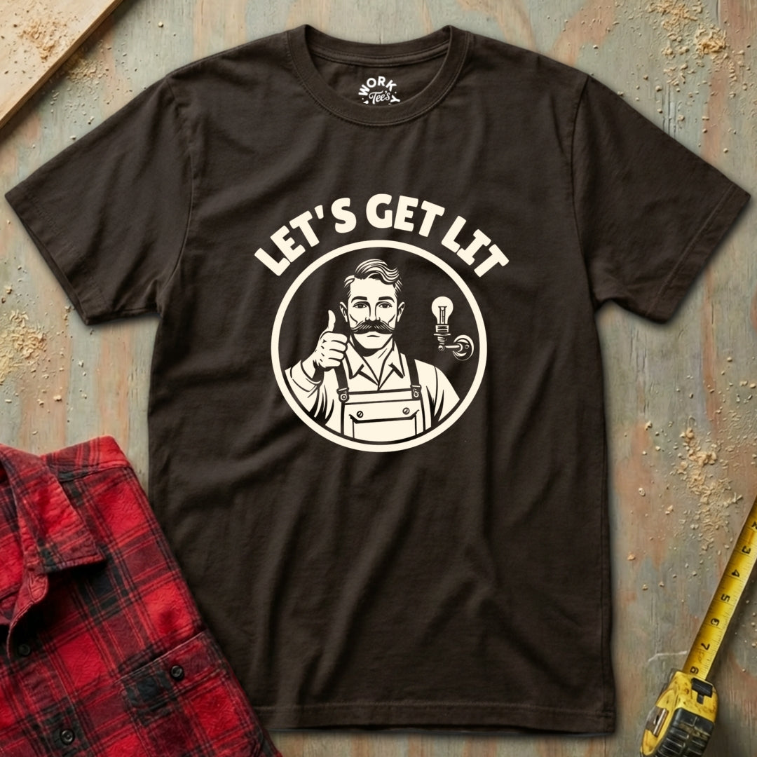 Brown t-shirt with 'Let's Get Lit' graphic design on a textured surface with a red plaid shirt and yellow tool in the background.