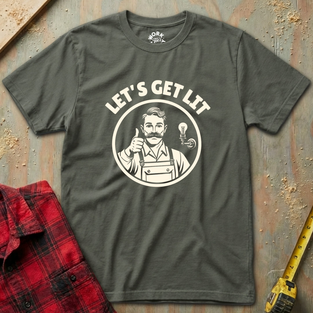 Gray t-shirt with 'Let's Get Lit' graphic design on a textured surface with a red plaid shirt and yellow tool in the background.
