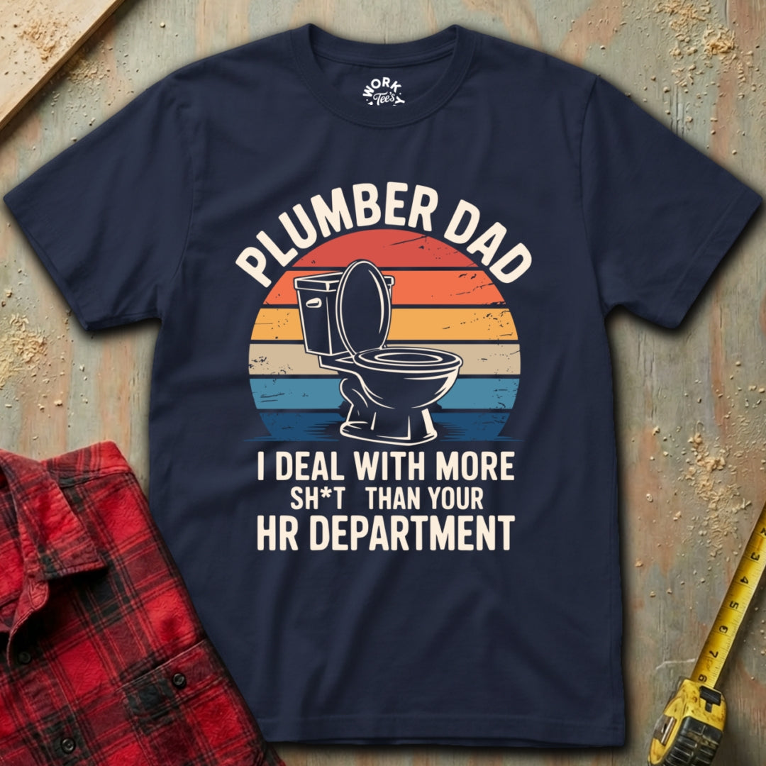 Navy blue t-shirt with 'Plumber Dad' graphic and text on a textured surface with tools.