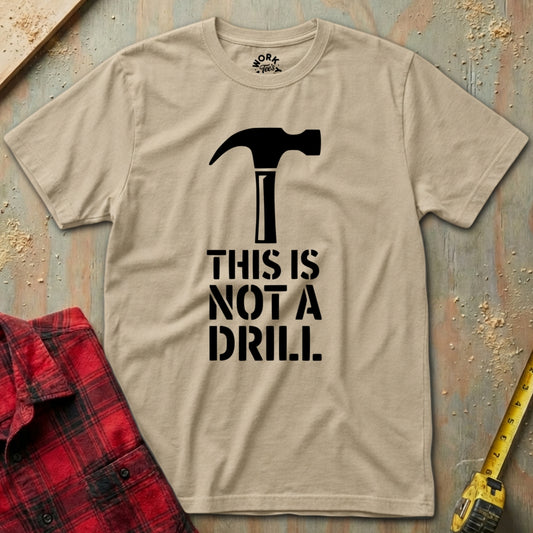 Beige t-shirt with a hammer graphic and 'This is not a drill' text on a wooden surface with tools.