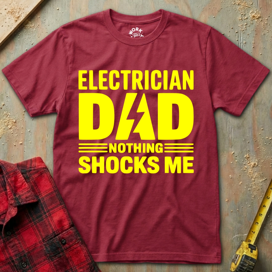 Maroon t-shirt with yellow text 'Electrician Dad Nothing Shocks Me' on a textured surface.