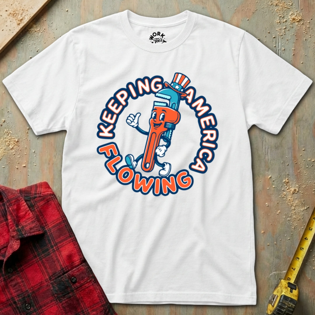 White t-shirt with a colorful graphic design on a textured surface with a red plaid shirt and yellow tool in the background.