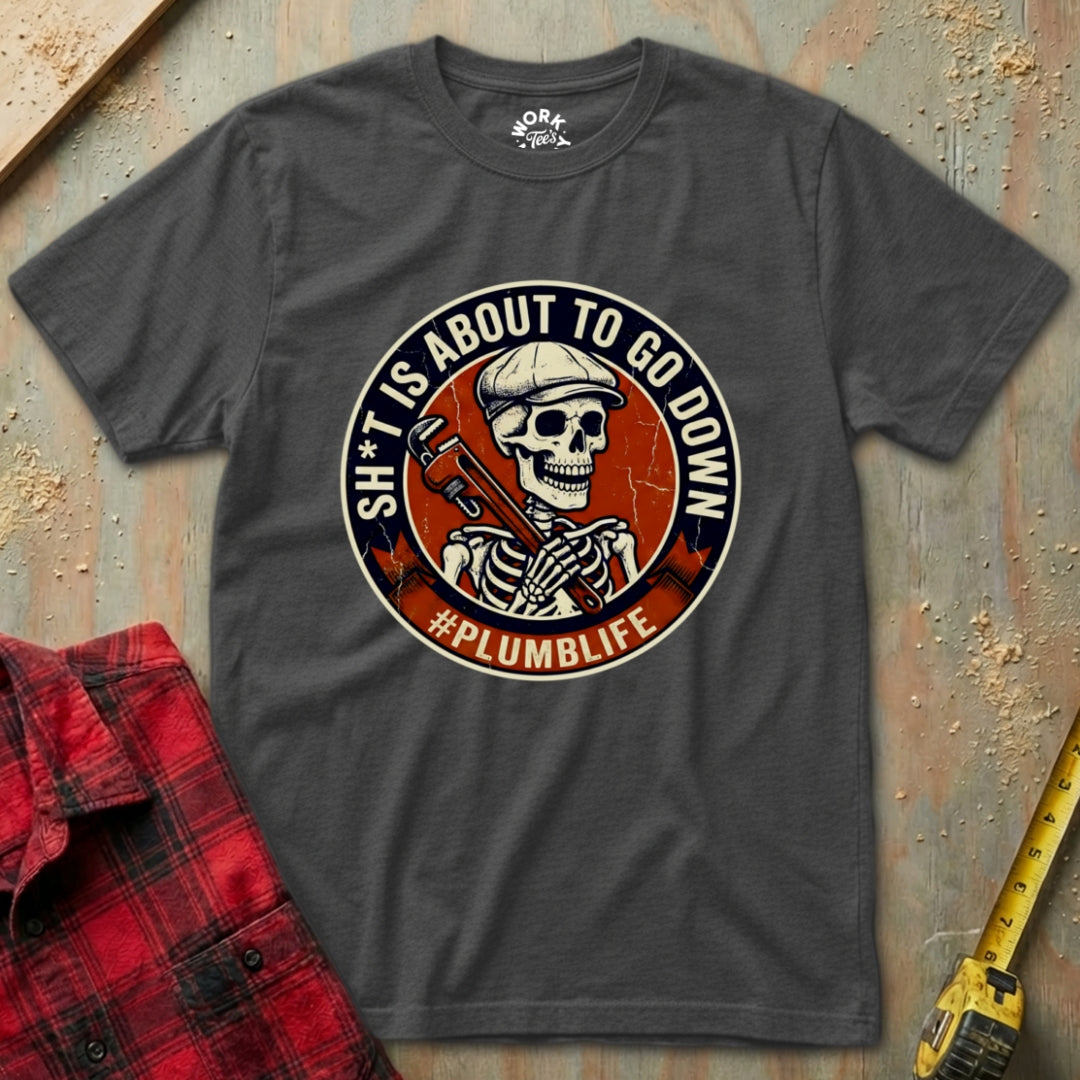 Gray t-shirt with a graphic design featuring a skeleton and text, placed on a wooden surface with a red plaid shirt and yellow tool in the background.